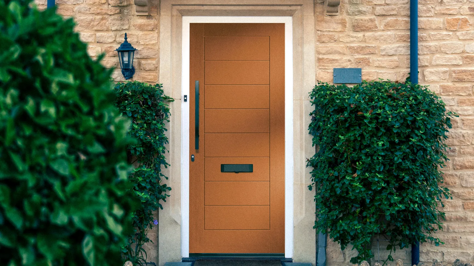 Contemporary oak-effect Clima63 door in a stone porch with evergreen planting