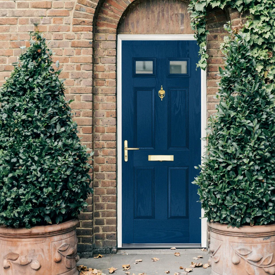 Navy Grandis44 four-panel door with gold furniture flanked by topiary trees against brick