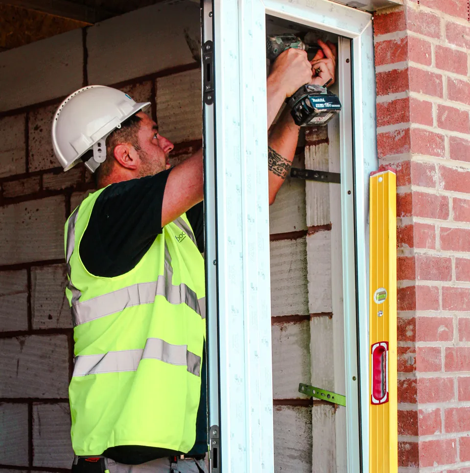 Installer in hard hat and hi-vis vest fixing a new door frame on a new-build housing site
