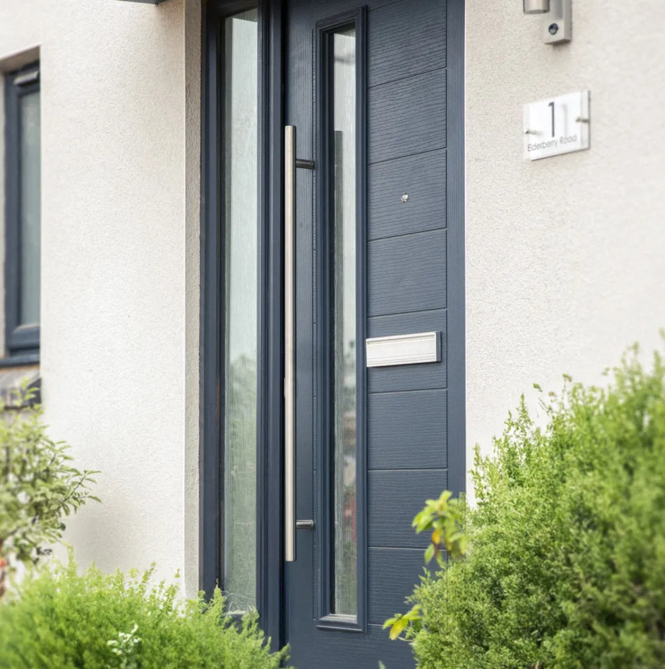 Finished dark grey composite front door with long bar handle and glazed side panel on a completed home