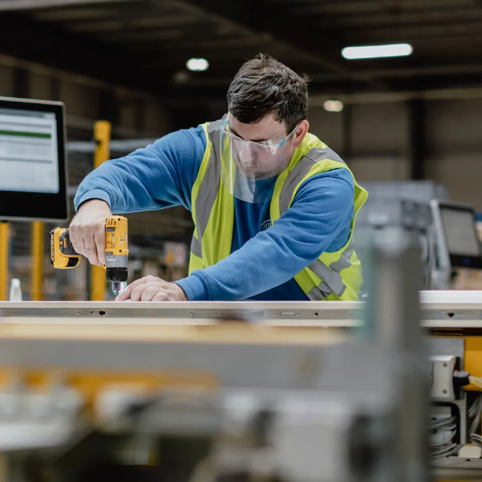 IG Doors factory worker in hi-vis and safety glasses fixing a door frame with a cordless drill
