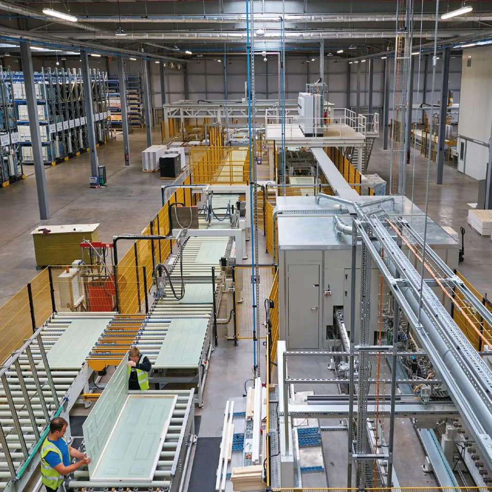 Door production line inside the IG Doors manufacturing facility, with workers handling door slabs on conveyors